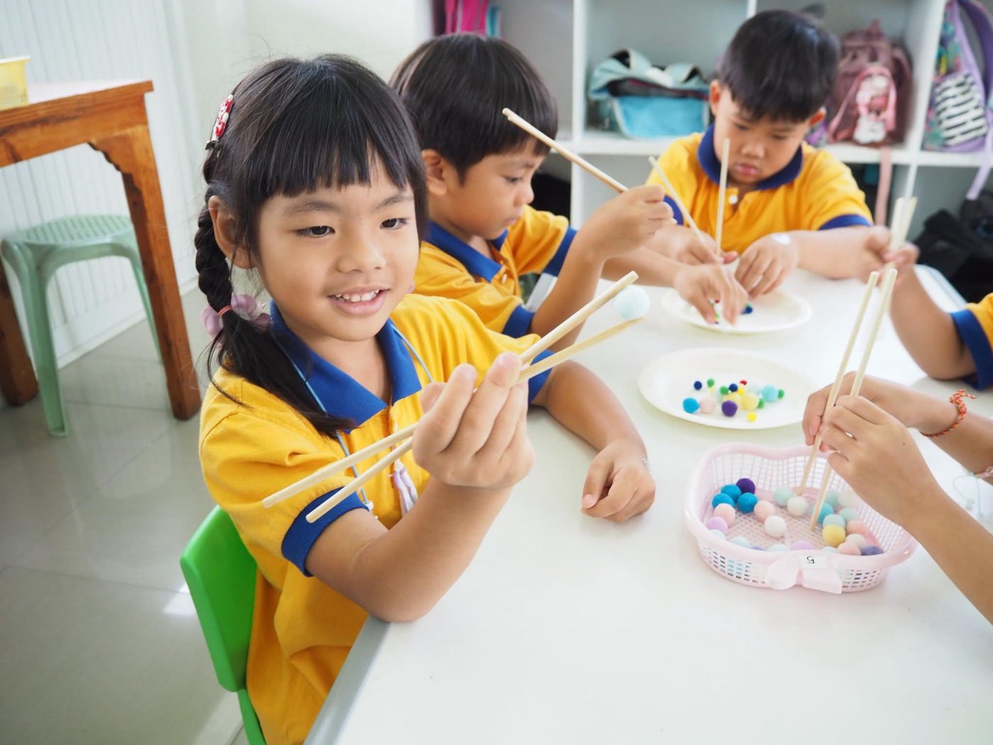 เด็กอนุบาล 1 ใช้ที่คีบหยิบลูกบอลสีอย่างตั้งใจ ฝึกกล้ามเนื้อมัดเล็กผ่านการเล่น
