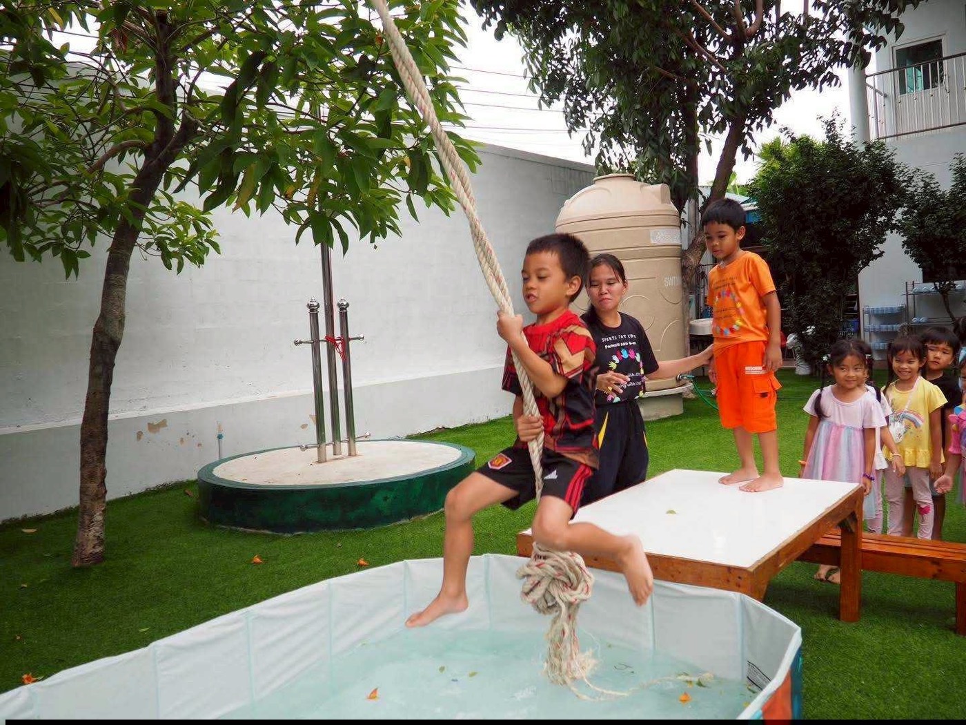 เด็ก ๆ เล่นเชือกโหนเหนือสระน้ำในสวนโรงเรียน
